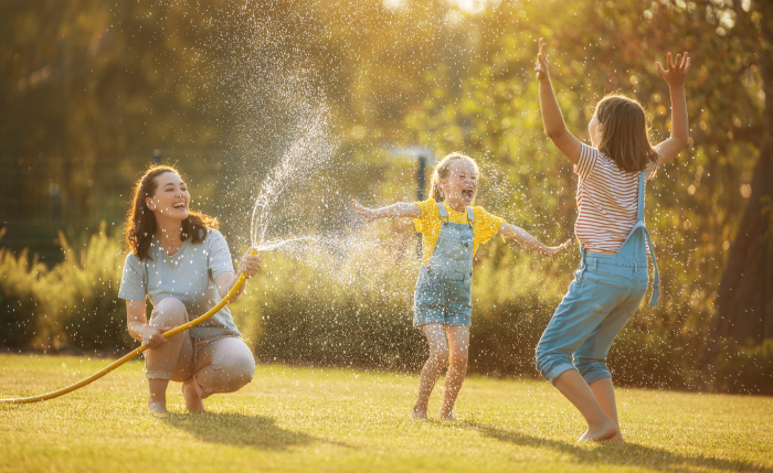 an image of a mother and her children playing with a hose one summer evening